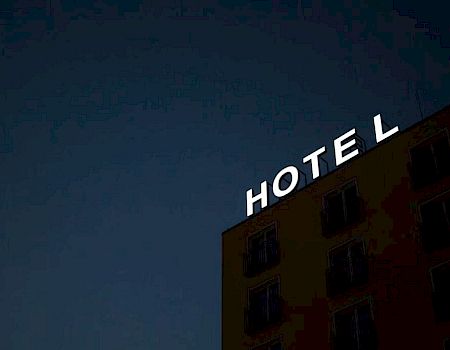 A hotel building with the word “HOTEL” lit on its roof against a dark blue twilight sky.