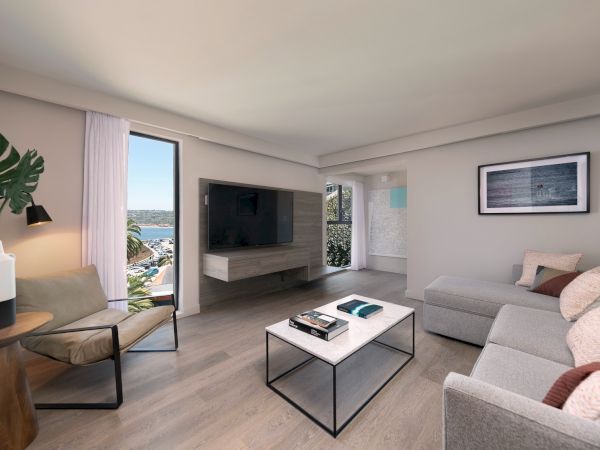 A bright, modern living room with a gray sectional sofa, glass coffee table, wall-mounted TV, stylish chair, plants, and large windows showing a coastal view.