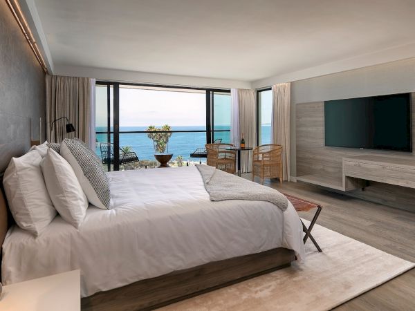 A modern hotel room with a large bed, wall-mounted TV, light wood tones, and a balcony overlooking the ocean&mdash;bright, airy, and relaxing.