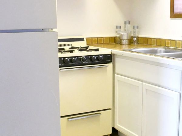A small white kitchen with a white fridge, stove, and cabinets, beige tile backsplash, and a sink by the window. End.