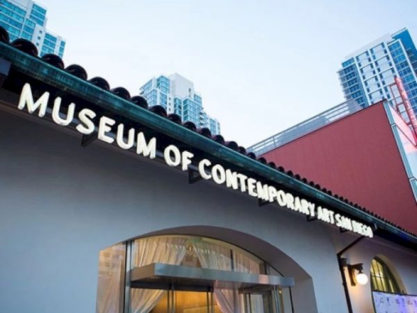 A building entrance sign reads &ldquo;Museum of Contemporary Design,&rdquo; with modern high-rise buildings in the background.