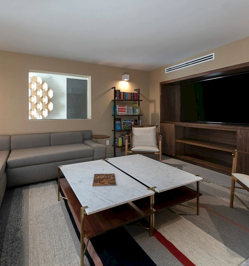 A modern lounge with a gray sectional sofa, marble coffee table, bookshelves, and a large wall-mounted TV, in warm light.