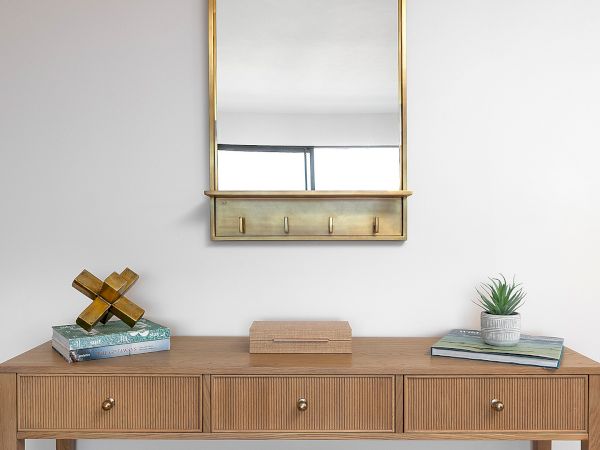 A simple entryway desk setup with a wooden console, a gold-framed wall mirror, cozy decor, and a small potted plant, neatly arranged.